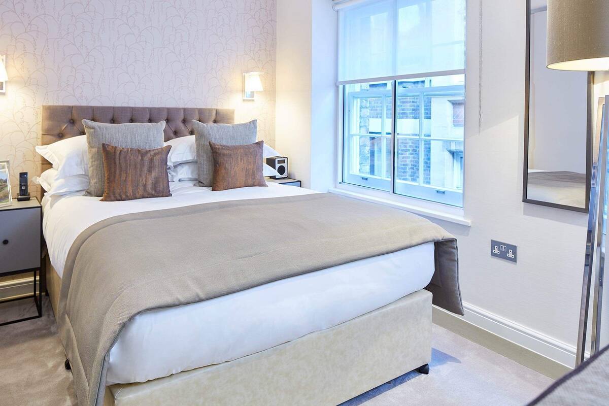 Une chambre à coucher bien aménagée, avec un grand lit, deux tables de chevet, une commode, une fenêtre donnant sur un beau paysage et une lampe fixée au mur.