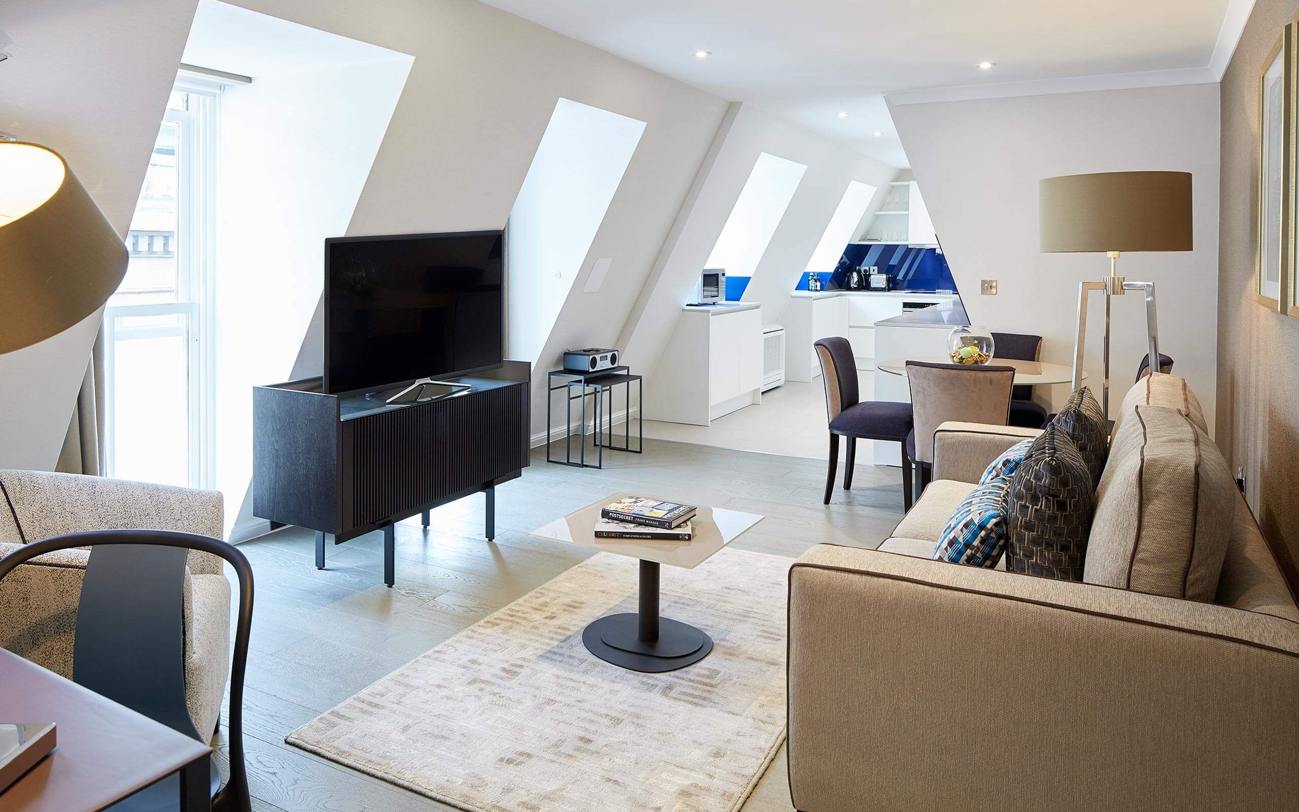 A modern living room with a flat-screen TV, a sofa, a coffee table, and a dining area with chairs.