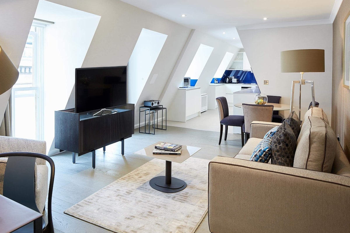 A modern living room with a flat-screen TV, a sofa, a coffee table, and a dining area with chairs.