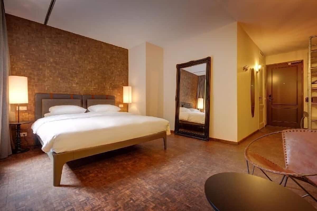 A hotel room with a large bed, a chair, a mirror, and a wardrobe.