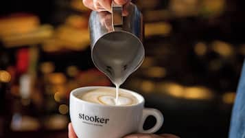 En person häller mjölk i en kopp som är märkt med texten ”stooker – specialkaffe”.