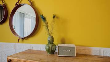 Un aparador de madera con un altavoz vintage Marshall y un florero verde con plantas secas, todo sobre un pared amarilla.