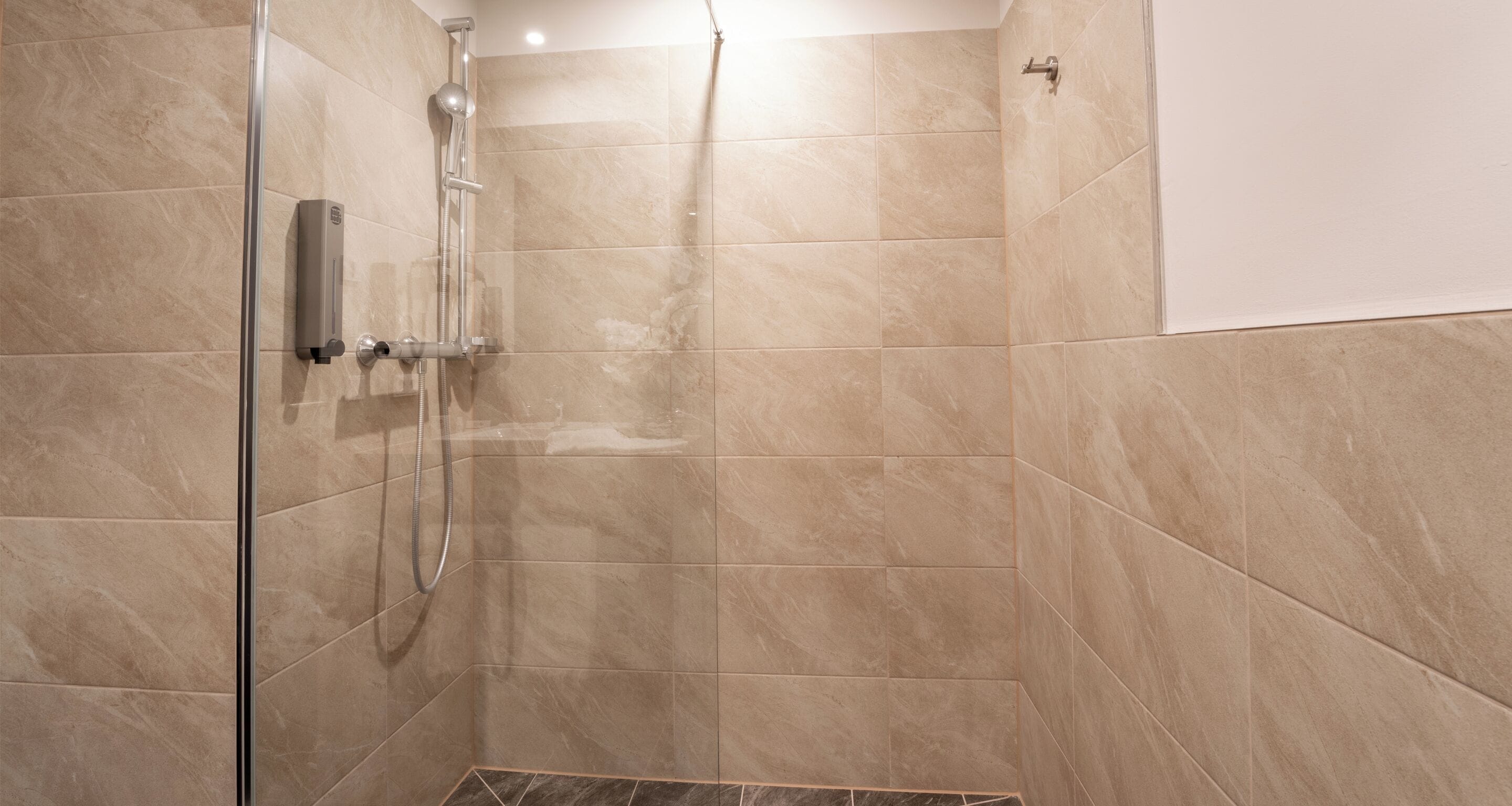 A modern bathroom with beige tiles, a glass shower enclosure, and a handheld showerhead.