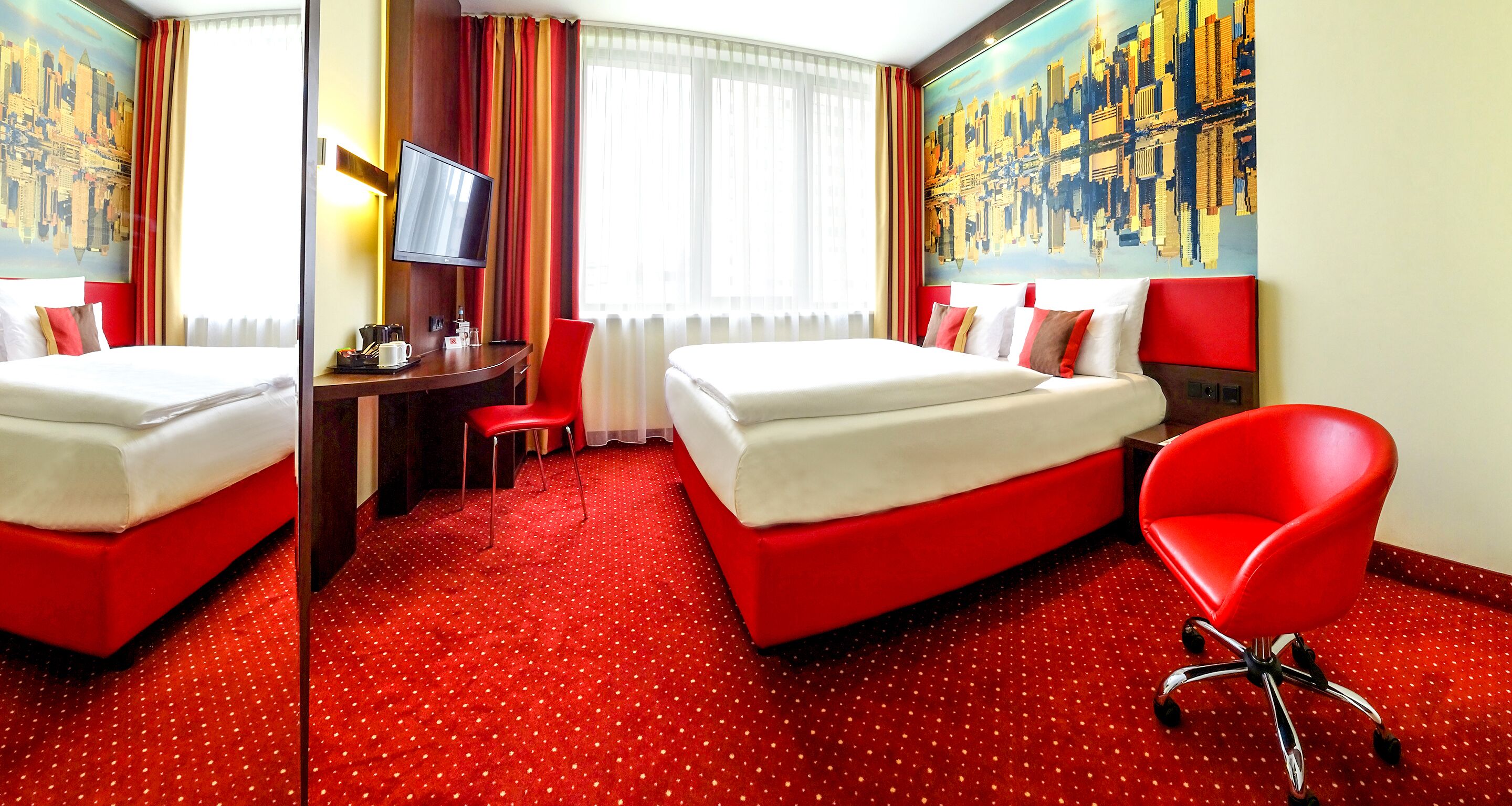 A hotel room with two beds, a desk, a chair, and a TV.