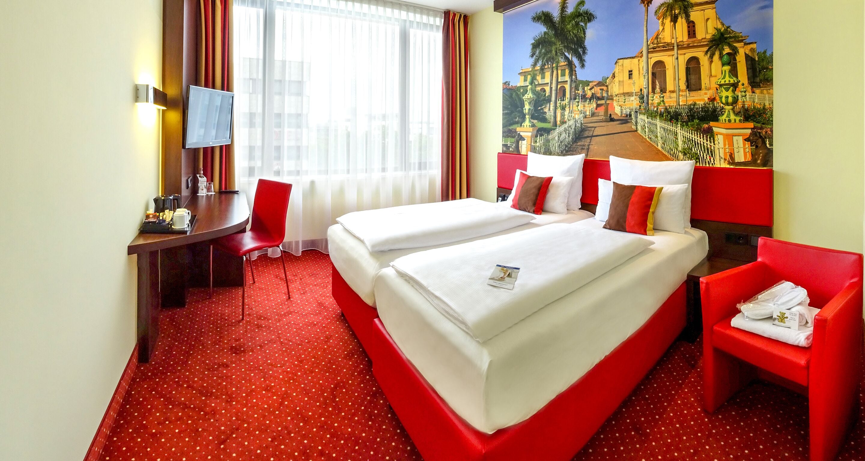 Habitación de hotel con dos camas, un escritorio, una silla y un ventanal con cortinas.