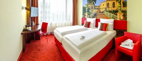Habitación de hotel con dos camas, un escritorio, una silla y un ventanal con cortinas.