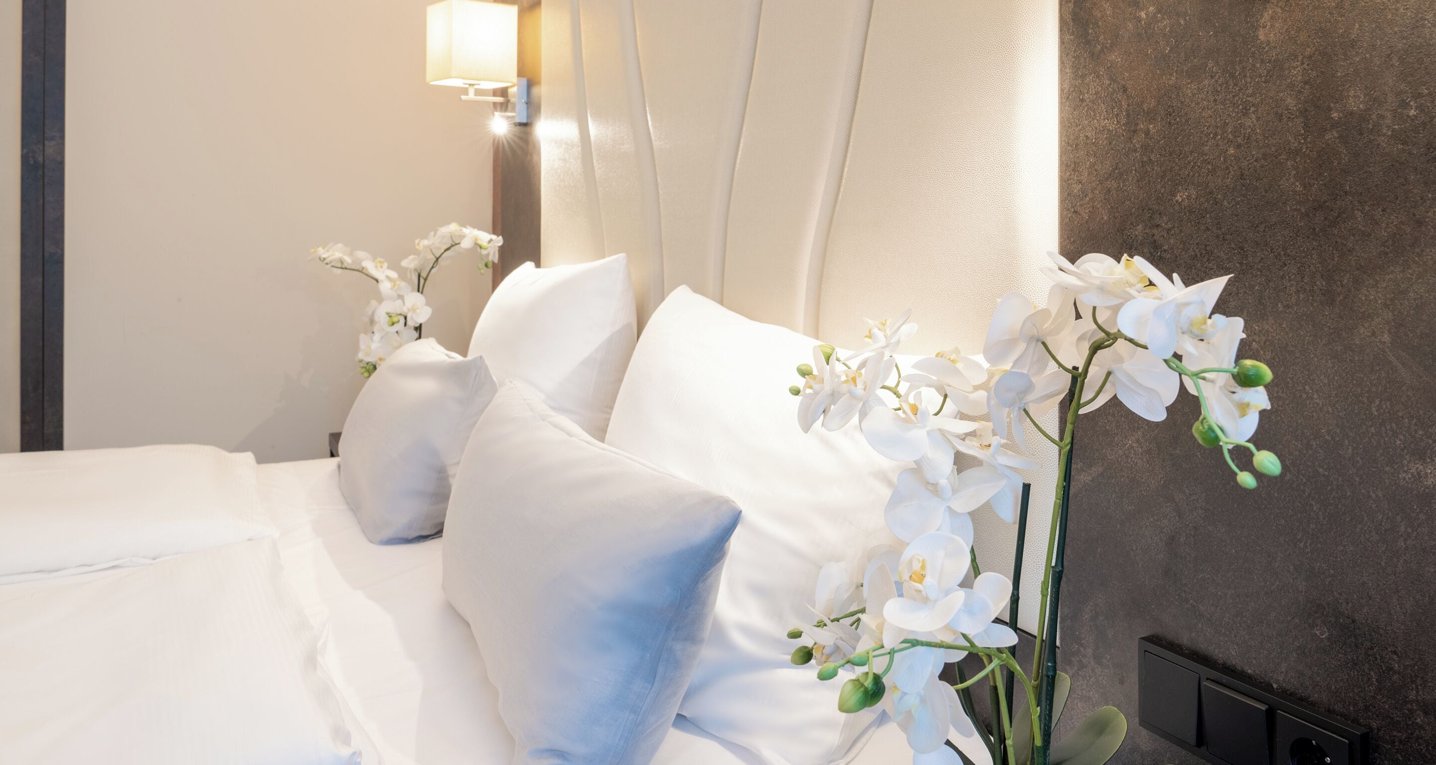 Un letto rifatto con lenzuola bianche e un vaso di orchidee bianche.