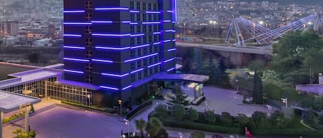 A modern hotel with a multi-story structure, a prominent entrance, and a view of a bridge and cityscape in the background.