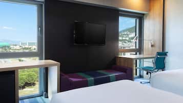 Una habitación de hotel moderna con una cama grande, un escritorio, una silla y un televisor montado en la pared.