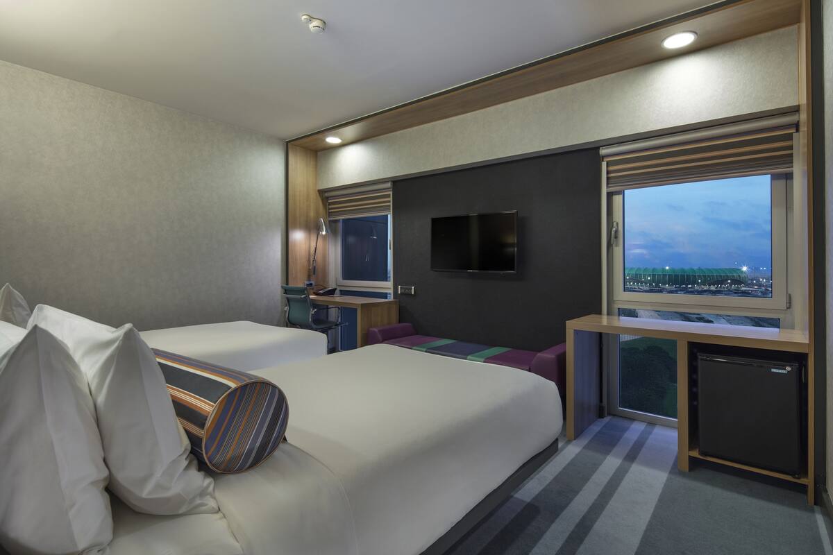 Ein modernes Hotelzimmer mit einem großen Bett, einem Schreibtisch, einem Fernseher und einem Fenster mit Blick auf die Stadt.