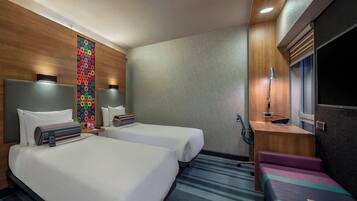 Habitación de hotel con dos camas, un escritorio, una silla, un televisor y una obra de arte colorida en la pared.