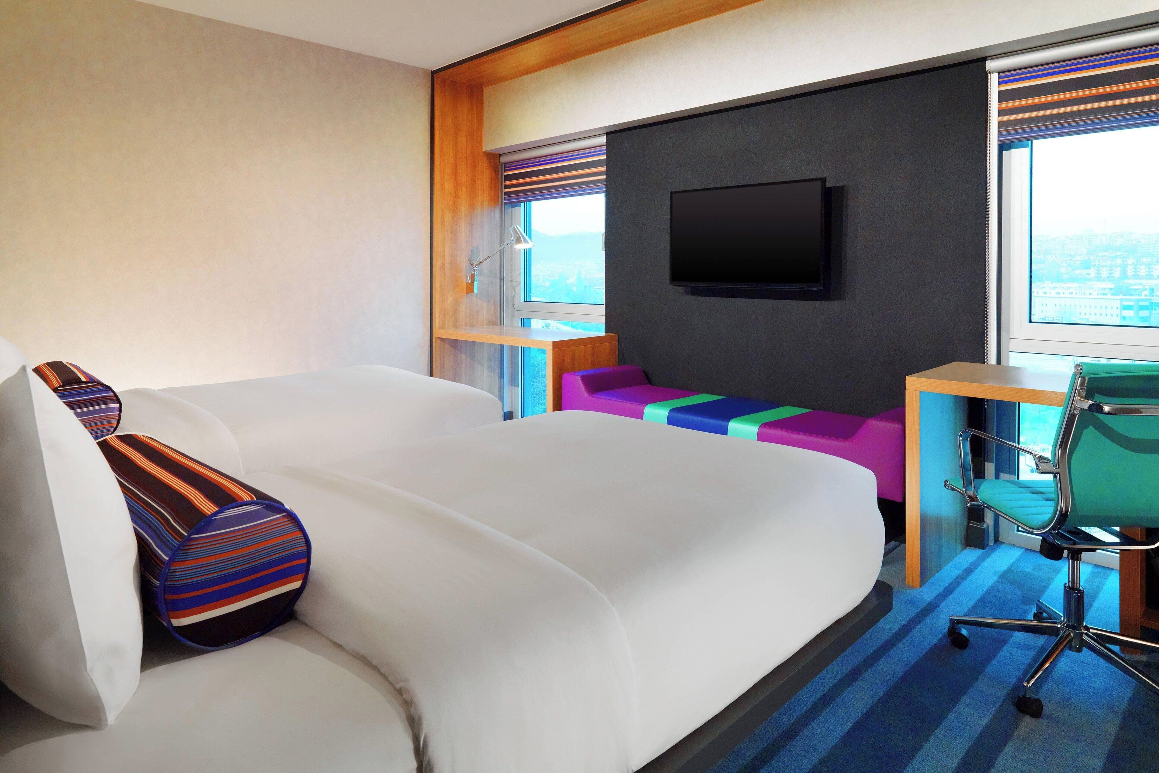 Una habitación de hotel con una cama grande, un escritorio con una silla, un televisor en la pared y una ventana con vista a la ciudad.