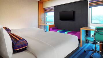 Una habitación de hotel con una cama grande, un escritorio con una silla, un televisor en la pared y una ventana con vista a la ciudad.