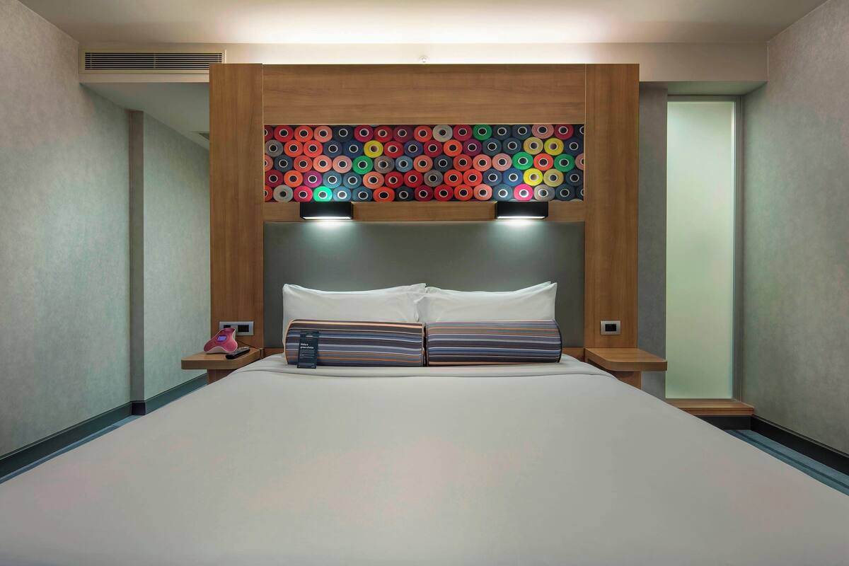 Une chambre d’hôtel moderne avec un grand lit, une tête de lit en bois et un décor mural circulaire aux couleurs vives.