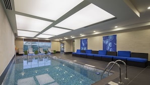A modern indoor swimming pool with clear water, a tiled floor, and blue cushioned seating along the walls. - Aloft by Marriott Bursa Hotel (Bursa)