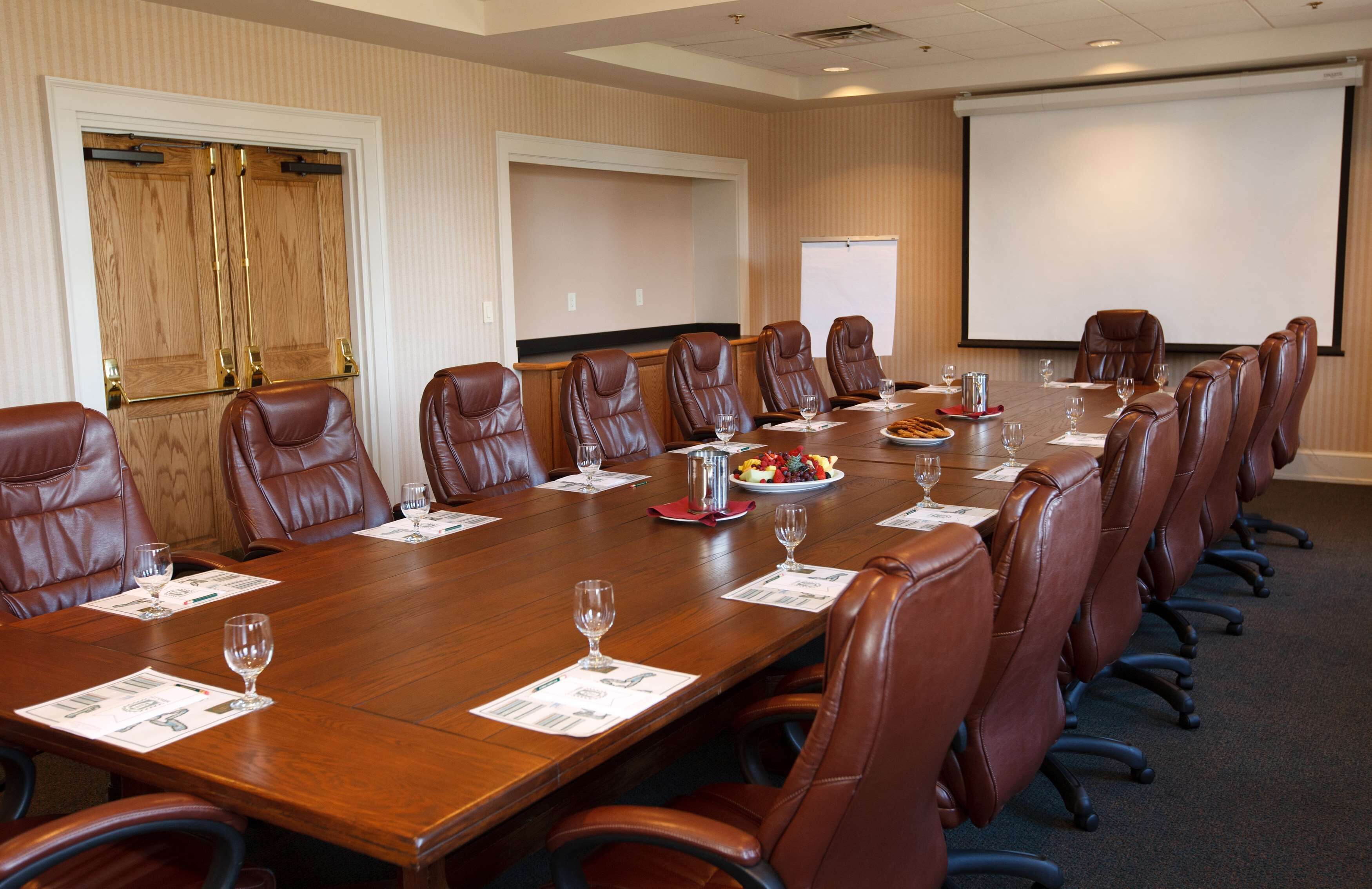 A conference room with a long table, leather chairs, a projector screen, and a whiteboard.