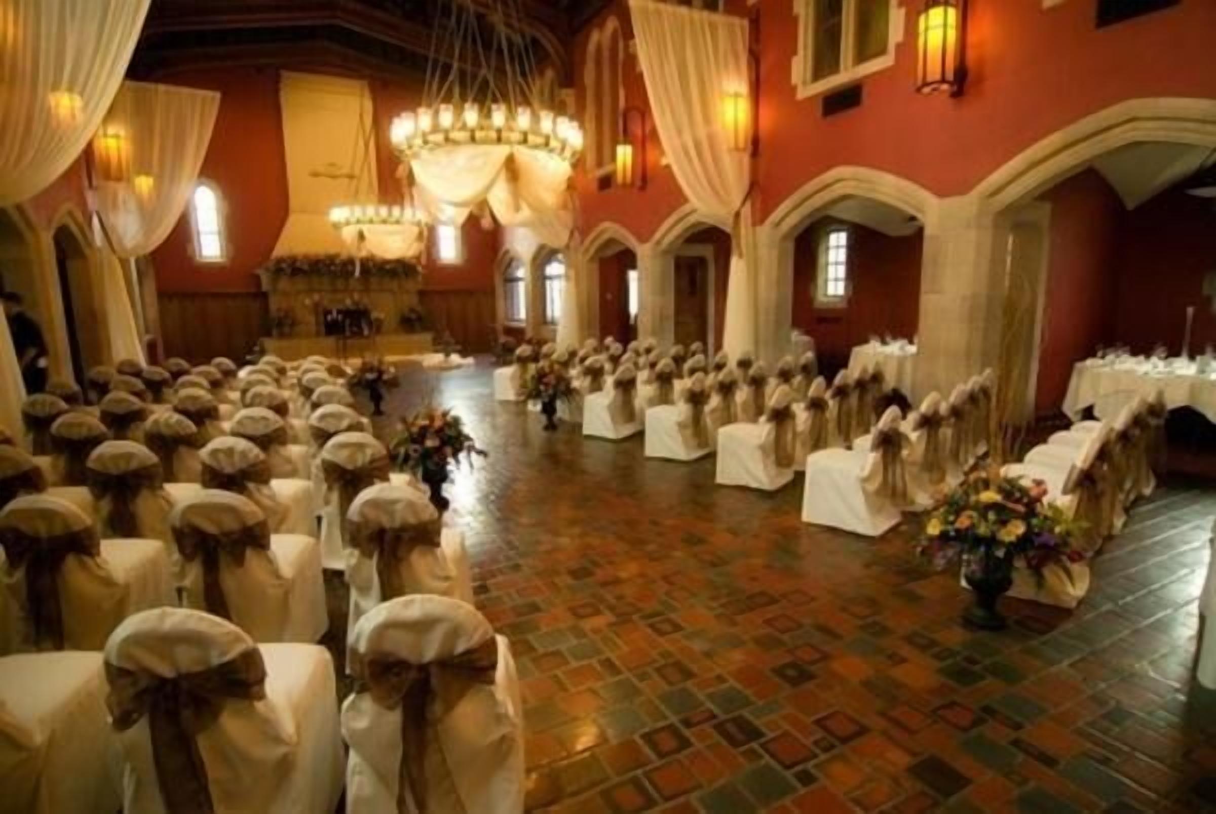 Un gran salón con filas de mesas y sillas, cubiertas con manteles blancos y decoradas con centros de flores.