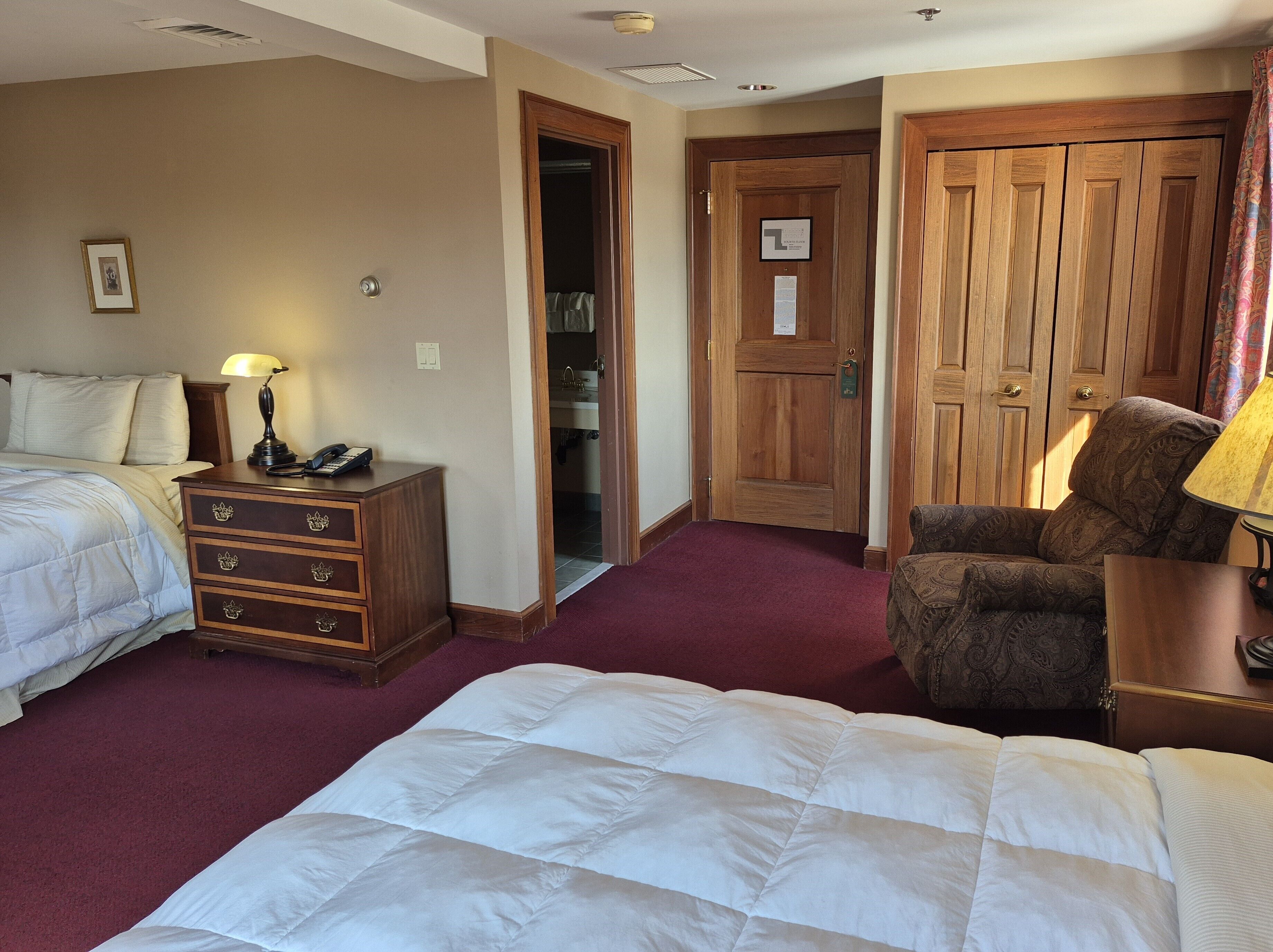 A hotel room with two beds, a wooden dresser, a chair, and a door leading to a bathroom.