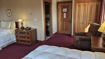 A hotel room with two beds, a wooden dresser, a chair, and a door leading to a bathroom.