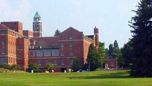 A large, historic building with a prominent clock tower, surrounded by well-maintained lawns and trees. - Bertram Inn at Glenmoor (Canton)