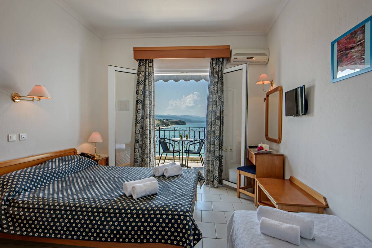 Une chambre d’hôtel avec deux lits, un bureau, une chaise, une télévision et un balcon donnant sur la mer.