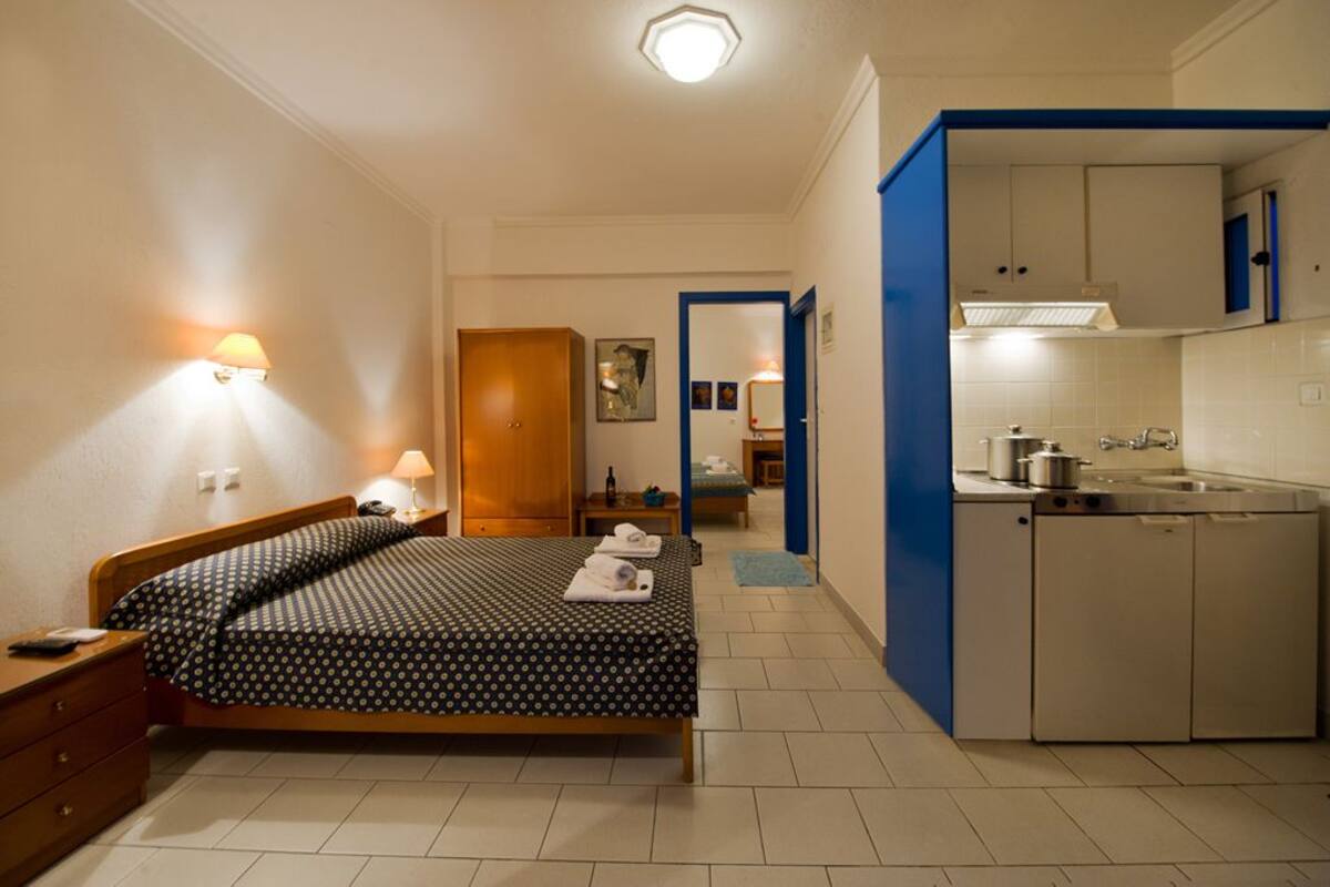 Une chambre d’hôtel de taille réduite, comprenant un lit, une table de chevet, une lampe et un coin cuisine.