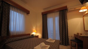 Een hotelkamer met een groot bed, twee opgerolde handdoeken, een bureau met een lamp en een spiegel.