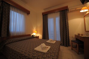 A hotel room with a large bed, two rolled towels, a desk with a lamp, and a mirror.