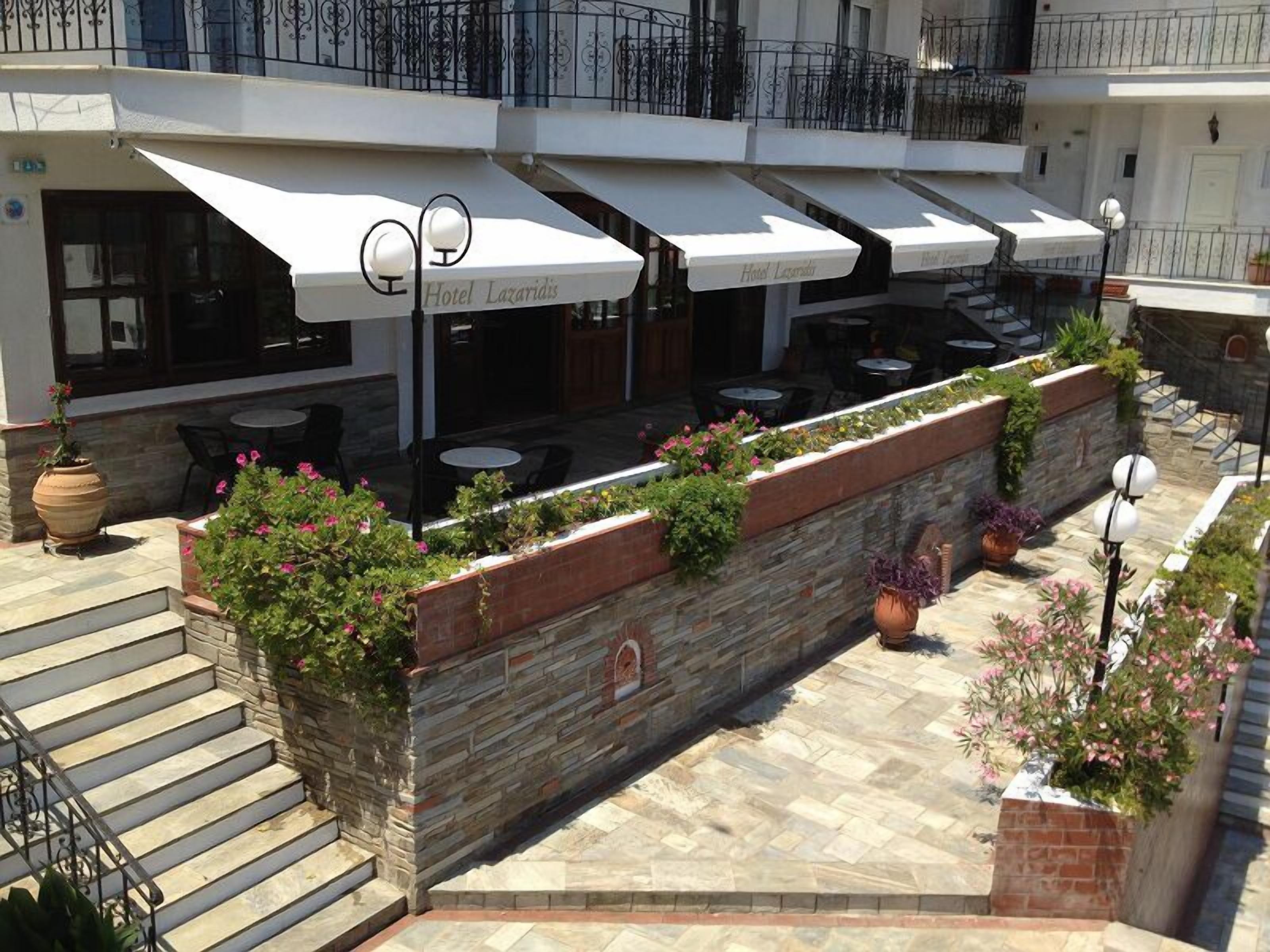 Un patio de hotel con mobiliario exterior, muros de piedra y plantas en macetas.