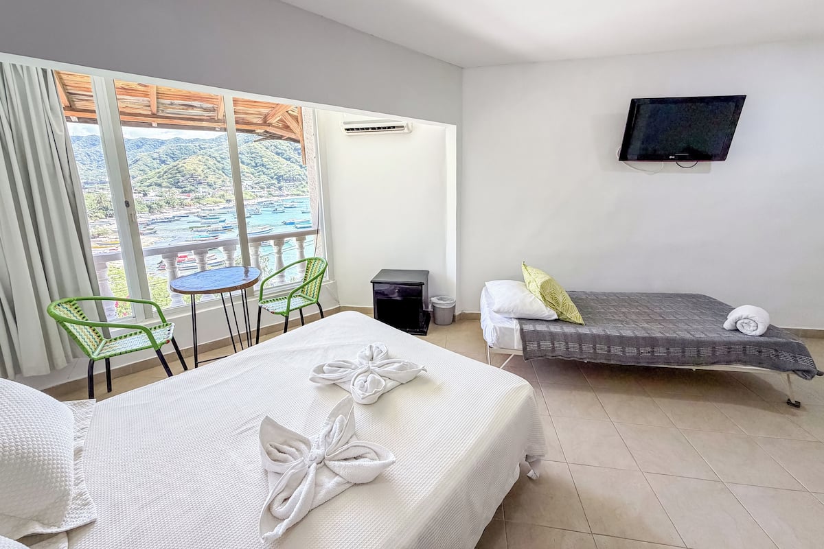 A hotel room with two beds, a TV, a balcony with a view, and a small table with chairs.