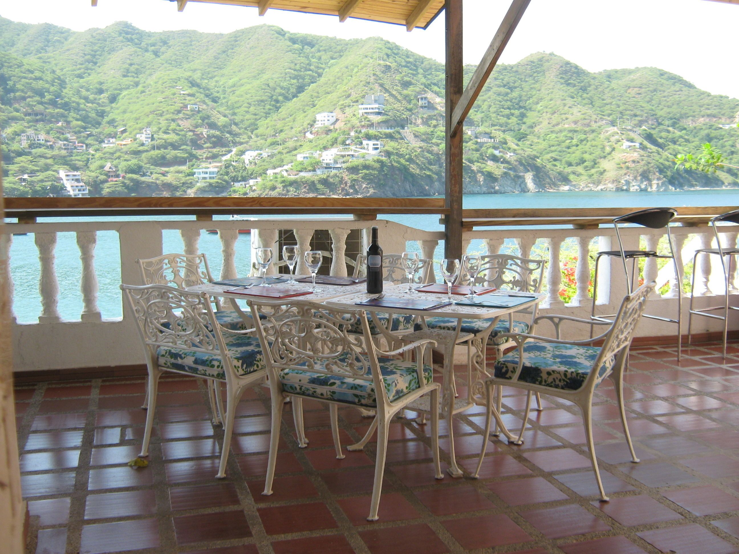 A terrace with a table set for dining, overlooking a mountainous landscape and a body of water.