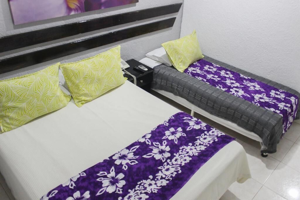 A hotel room with two beds, each with a distinct floral bedspread, a flat-screen TV mounted on the wall, and a telephone on the nightstand.