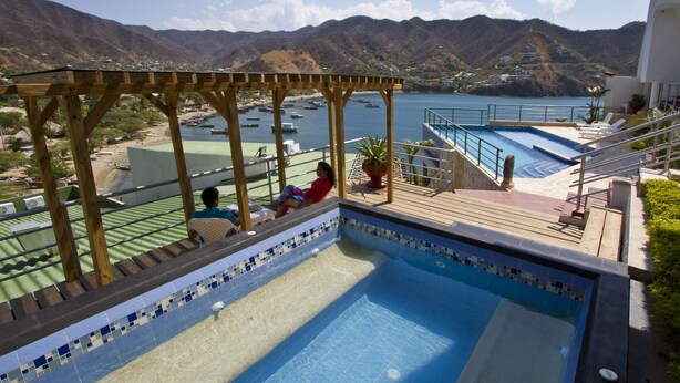 Ein Pool mit Blick auf Boote auf dem Wasser, einer Holzterrasse und einem Berg im Hintergrund.