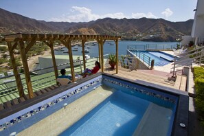 Une piscine avec vue sur les bateaux qui flottent sur l’eau, une terrasse en bois et une chaîne de montagnes en arrière-plan.