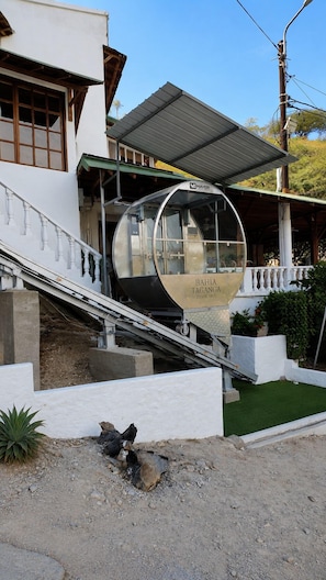 Un edificio moderno con un área exterior cubierta, una estructura cilíndrica y una escalera que lleva a un edificio blanco.