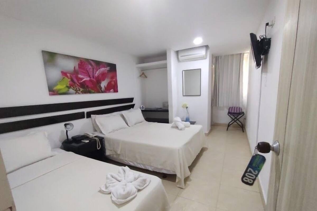 A hotel room with two beds, a painting of flowers, an air conditioner, a TV, and a door with a number sign.