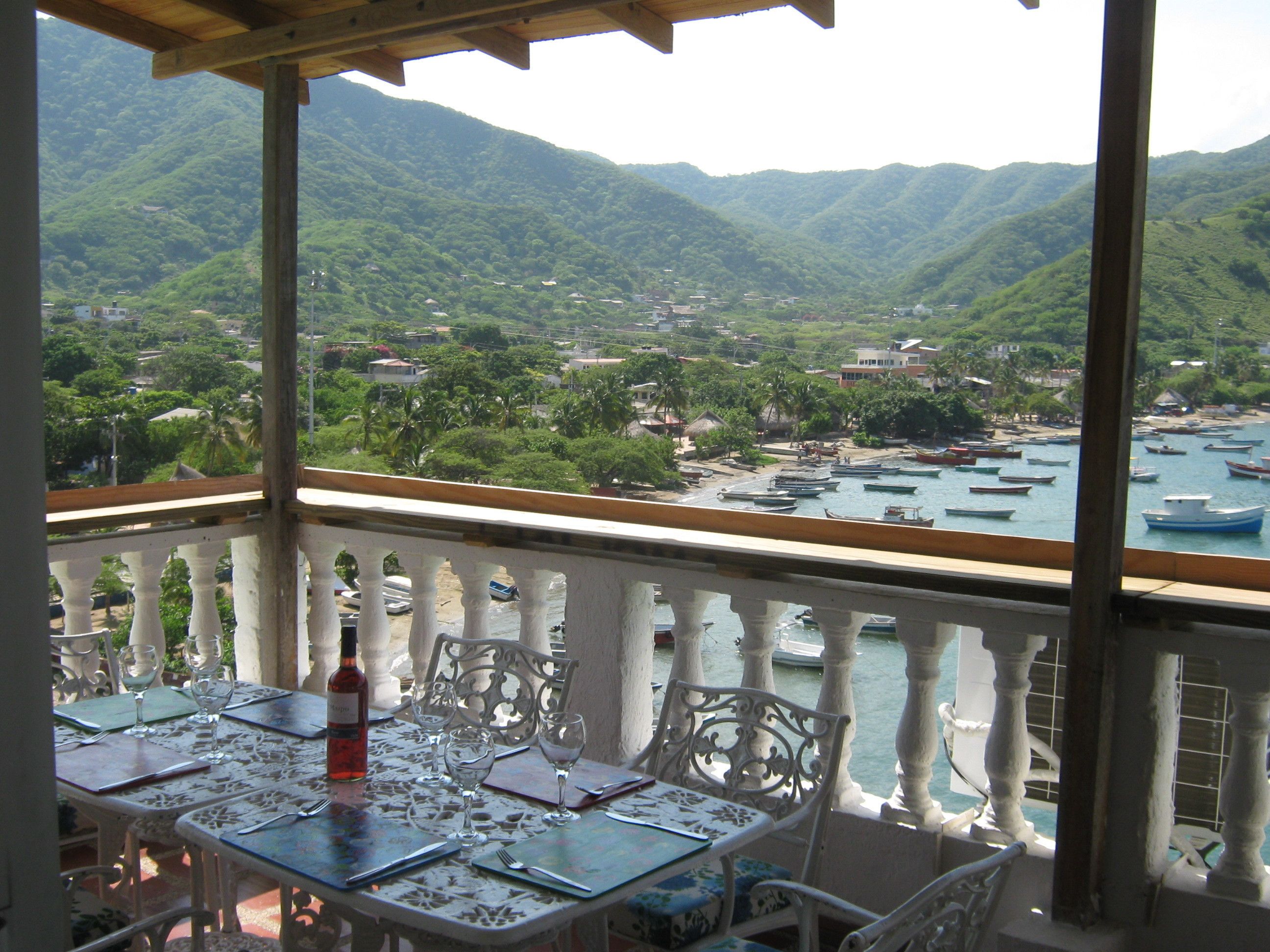 Un balcon avec une table dressée pour le dîner, donnant sur une baie où se trouvent des bateaux et un paysage montagneux.