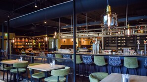 Un interior de restaurante moderno con sillas tapizadas en verde, mesas de madera y lámparas colgantes.