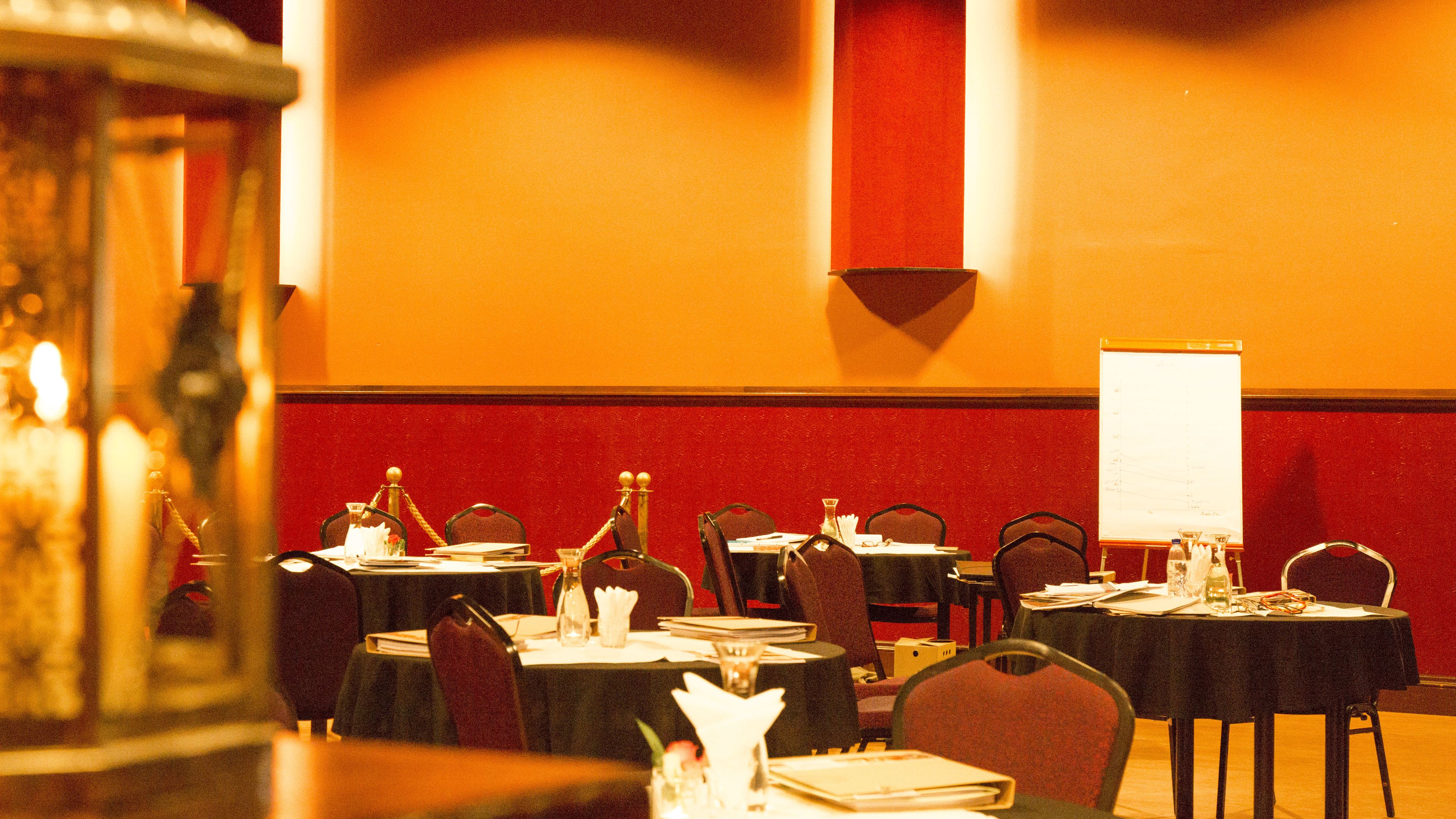Un salón de conferencias con mesas dispuestas para reuniones, una pizarra y una pared roja.