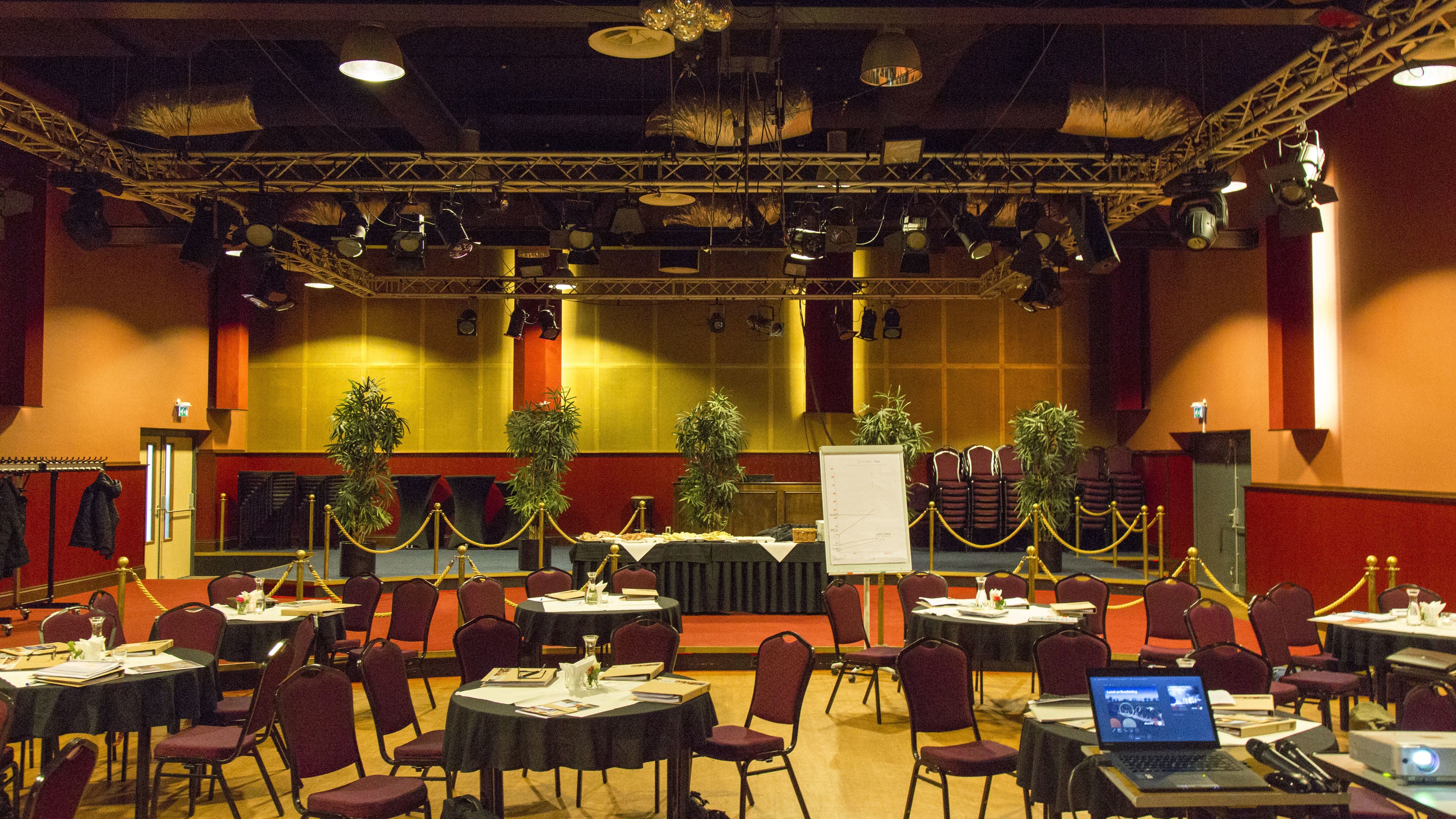A conference room with tables, chairs, and a stage with a whiteboard.