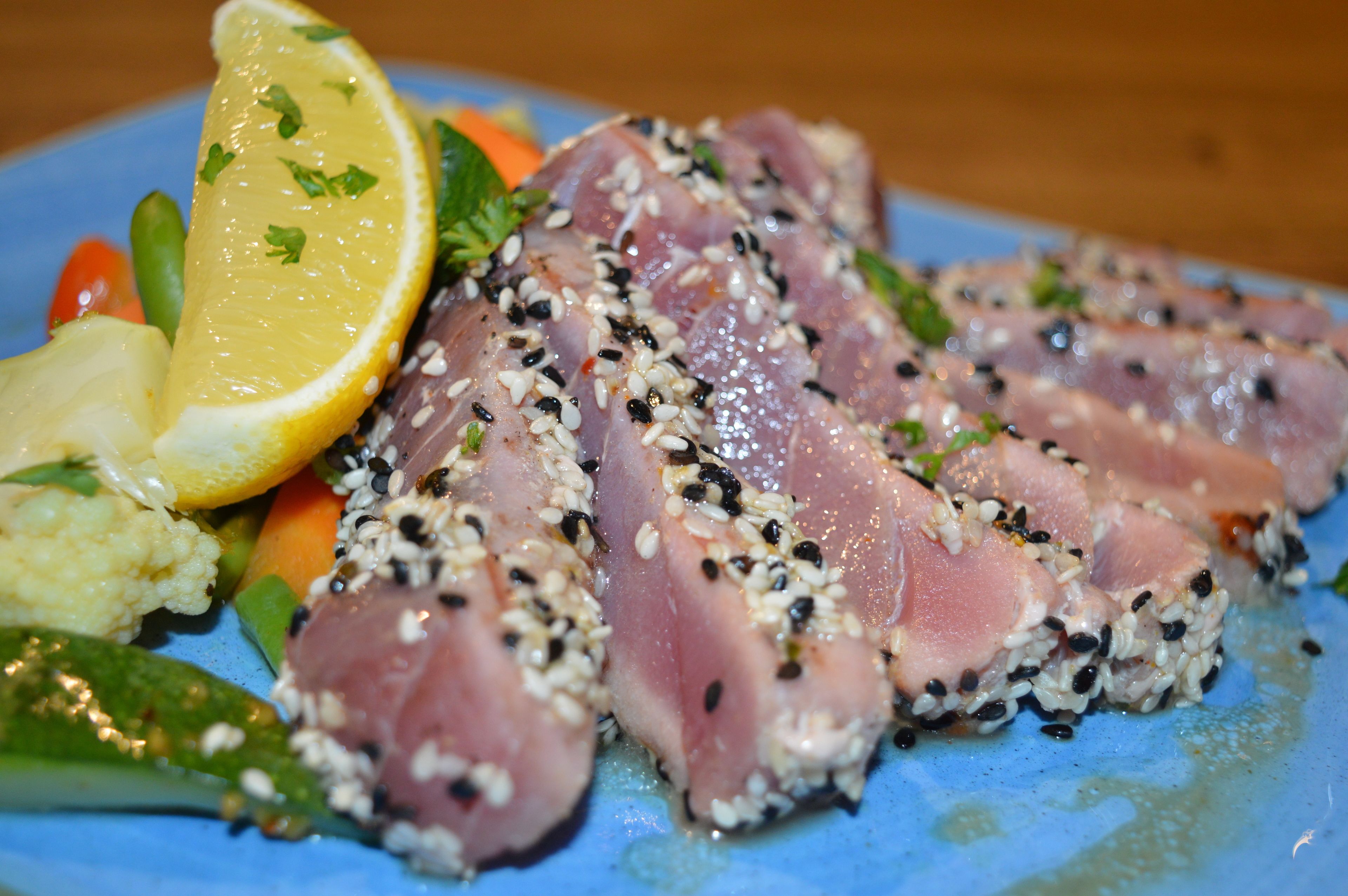 Een bord sashimi met sesamzaadjes, citroen en groenten.
