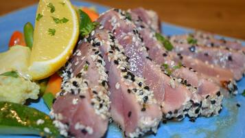 Een bord sashimi met sesamzaadjes, citroen en groenten.