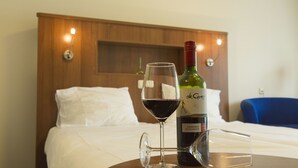 Una cama con sábanas blancas, una botella de vino y una copa de vino tinto sobre una mesita.