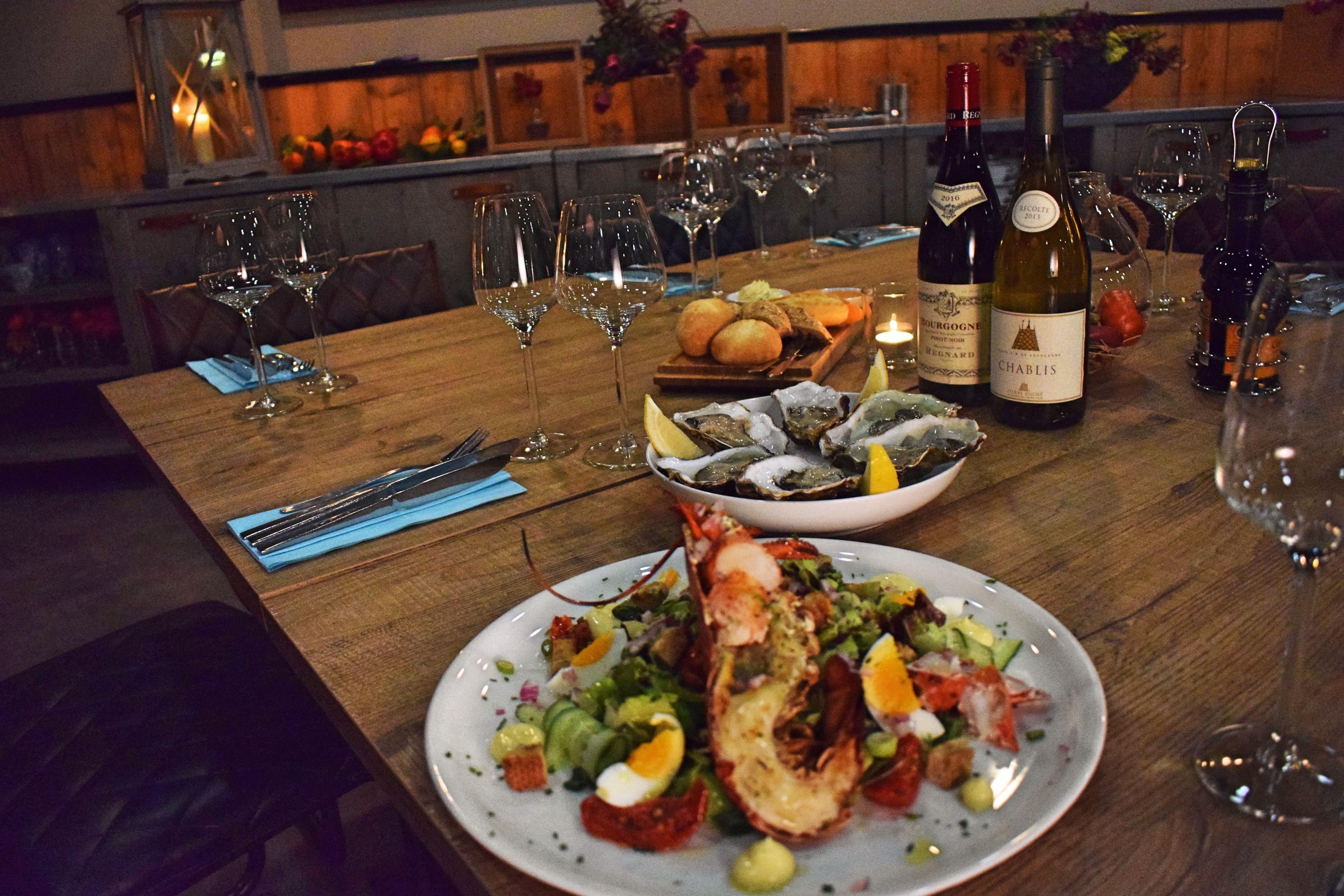 Uma mesa de jantar posta com taças de vinho, garrafa de vinho, frutos do mar e pão.
