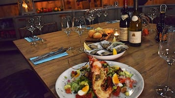 Uma mesa de jantar posta com taças de vinho, garrafa de vinho, frutos do mar e pão.