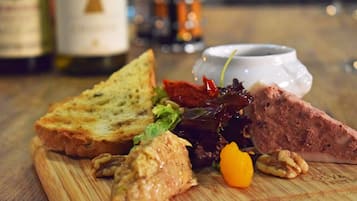A wooden cutting board with various food items including bread, meat, nuts, and a small yellow fruit.