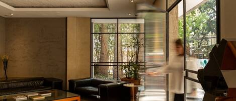 Un hall d’entrée moderne avec une table basse en verre, des canapés en cuir et une grande fenêtre donnant sur les arbres.