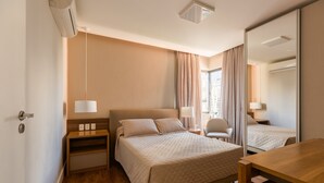 A hotel room with a bed, bedside tables, a desk, a chair, and a large mirror. - Alameda Apart Hotel (São Paulo)