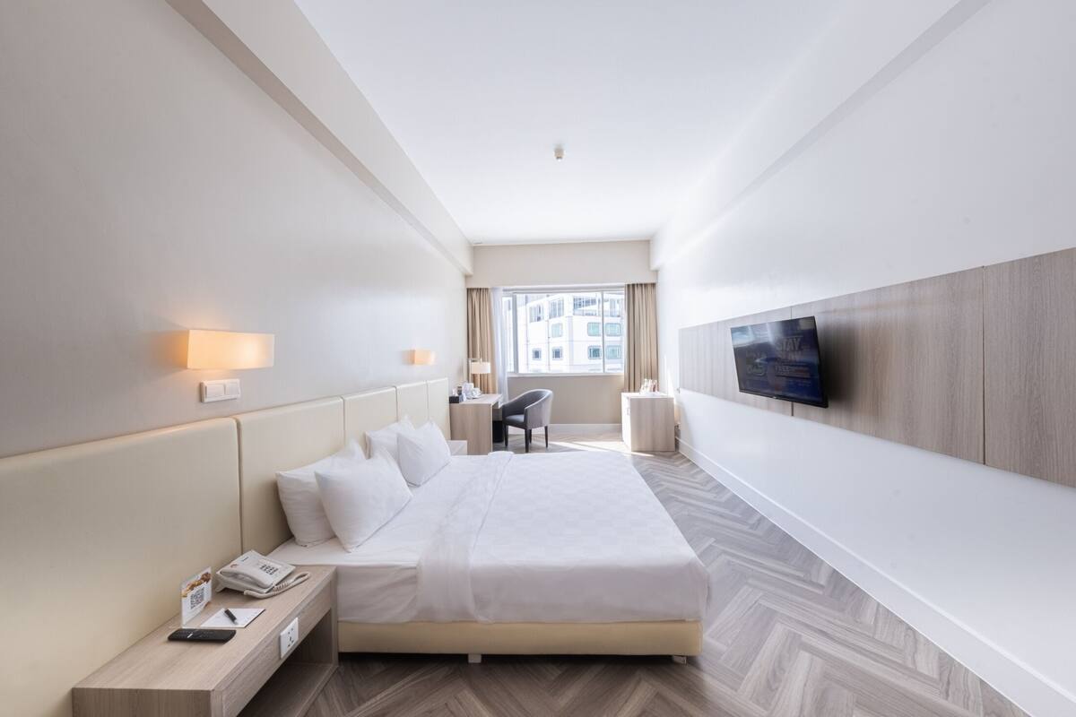 Una habitació d'hotel moderna amb un llit gran, taules de nit, un escriptori, una cadira i un televisor penjat a la paret.