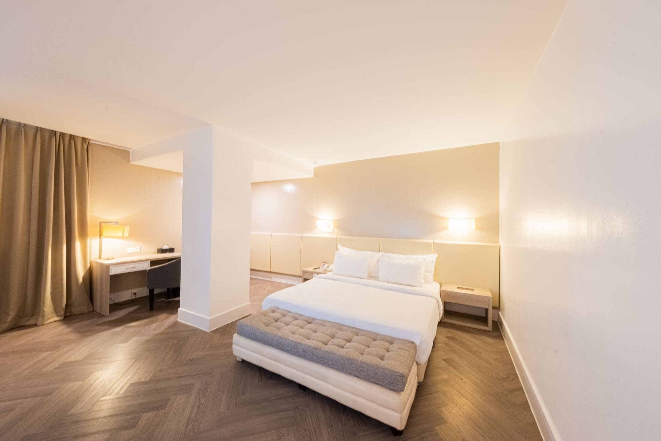A hotel room with a bed, bedside tables, a desk, and a chair.